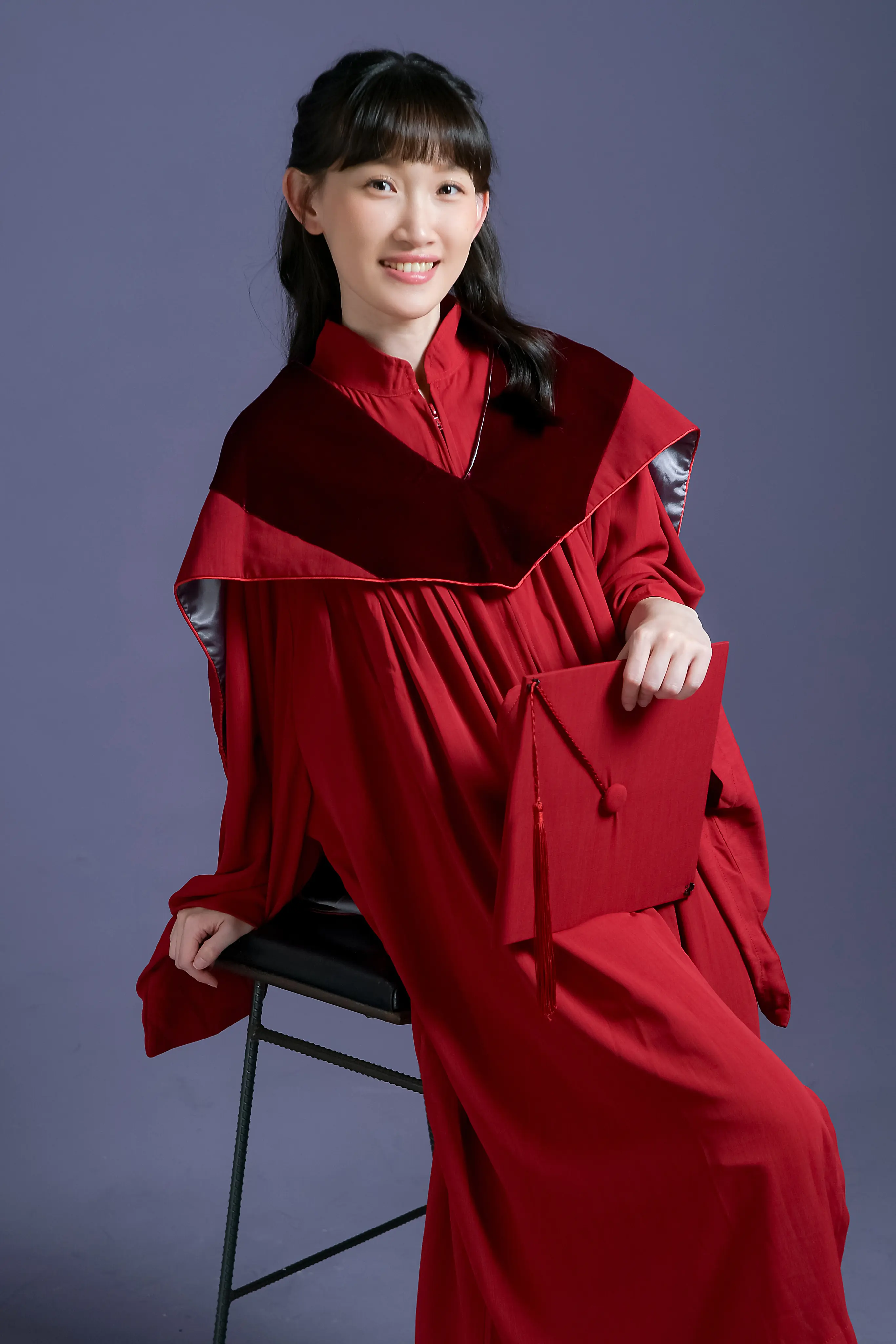 女兒穿紅色學士服手持畢業證書坐姿紀念照，記錄人生重要成長時刻